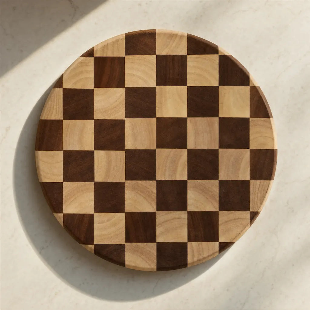 Top-down photograph of a circular ALORIVO Sapele wood cutting board with a hand-joined end-grain chessboard precision pattern, illuminated by bright natural light on a light marble kitchen counter.