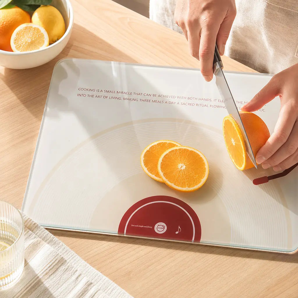 Cinematic close-up of Alorivo Dual-Fresh vinyl-inspired glass art board on a sun-drenched wooden countertop, hands slicing a fresh orange under natural California morning light, showcasing premium reflective texture and minimalist kitchen aesthetic.