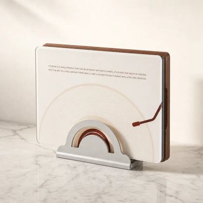 The complete Alorivo Dual-Fresh Cutting Board Set presented as an interior sculpture on a luxury white marble kitchen counter. The square vinyl-inspired glass board and the heavy Sapele wood board stand vertically inside a sleek metal architectural base, bathed in warm, cinematic morning light.