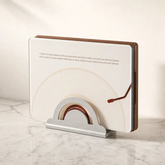 The complete Alorivo Dual-Fresh Cutting Board Set presented as an interior sculpture on a luxury white marble kitchen counter. The square vinyl-inspired glass board and the heavy Sapele wood board stand vertically inside a sleek metal architectural base, bathed in warm, cinematic morning light.